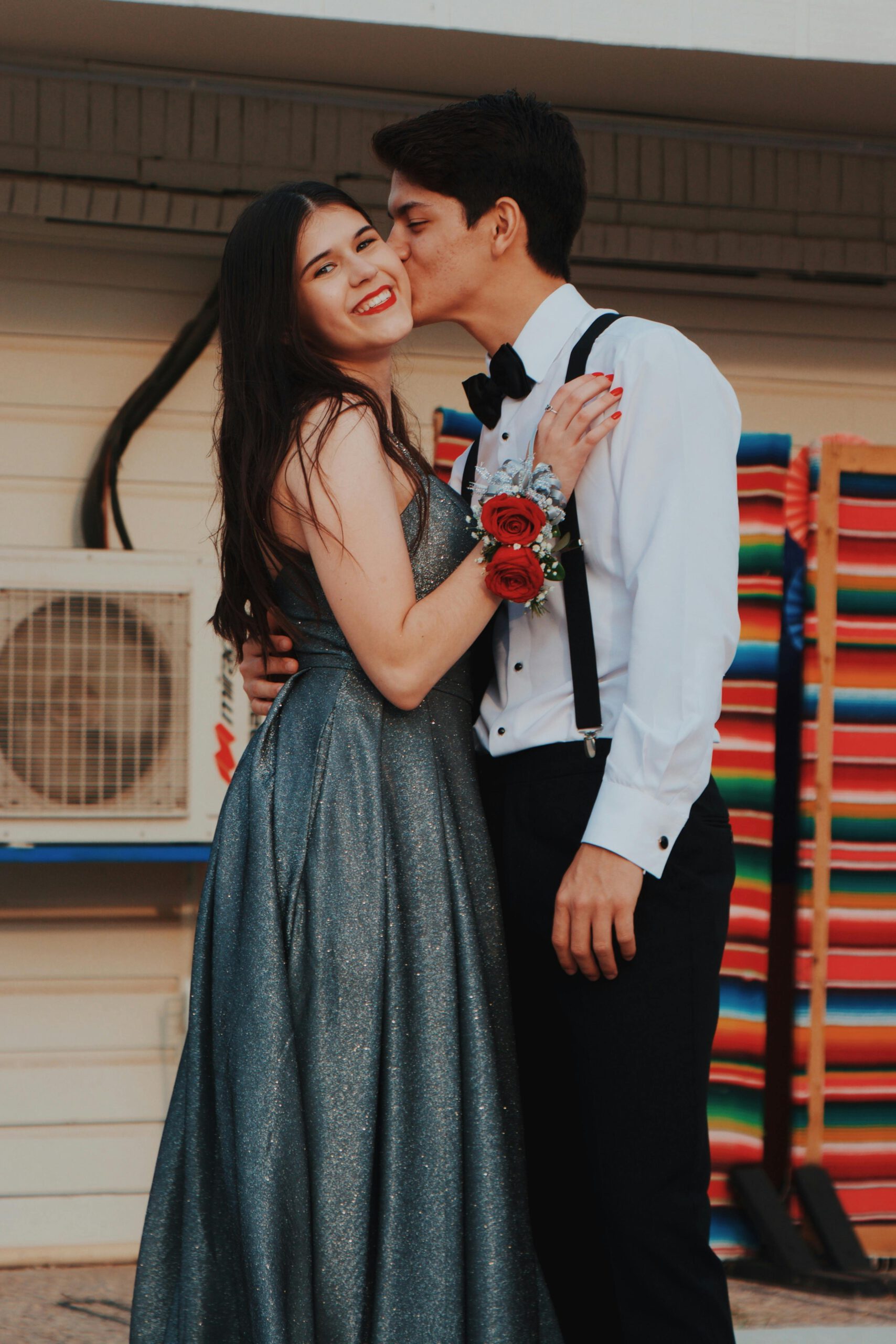 A smiling couple in formal attire shares a joyful embrace outdoors at sunset.